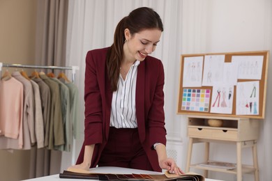 Photo of Fashion designer choosing fabric among colorful samples at white table in workshop