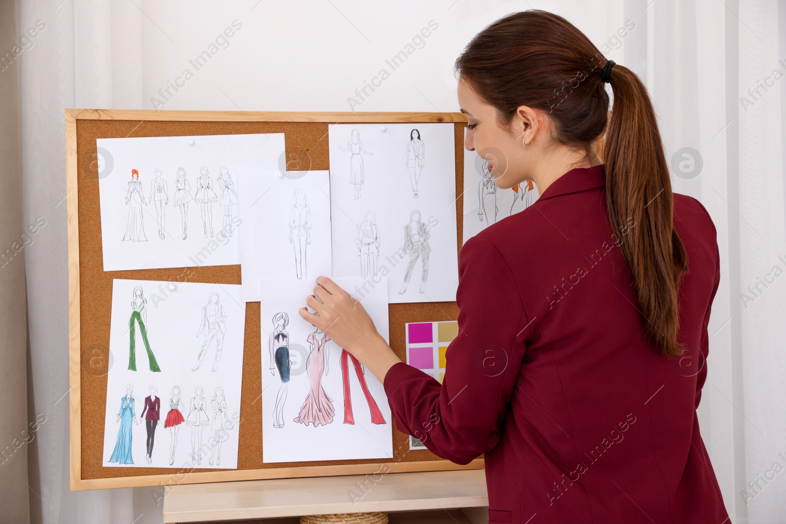 Photo of Fashion designer pinning sketch of clothes to corkboard in workshop