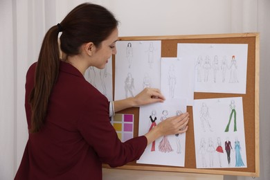 Photo of Fashion designer pinning sketch of clothes to corkboard in workshop