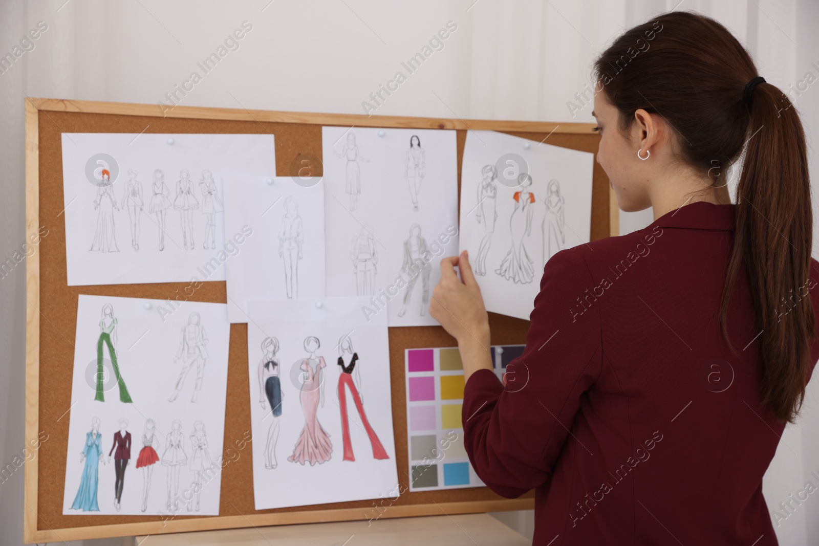 Photo of Fashion designer pinning sketch of clothes to corkboard in workshop