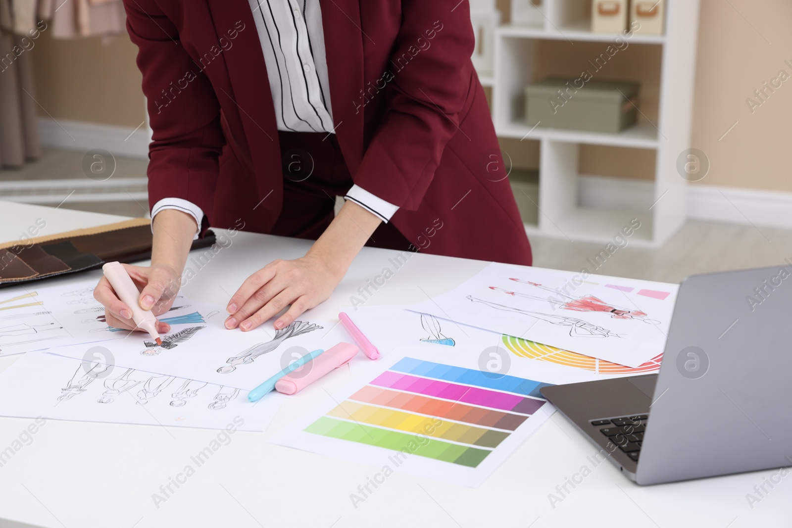 Photo of Fashion designer drawing sketch of clothes at white table in workshop, closeup