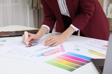 Photo of Fashion designer drawing sketch of clothes at white table in workshop, closeup