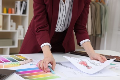 Photo of Fashion designer with sketches of clothes and color palettes working at white table in workshop, closeup