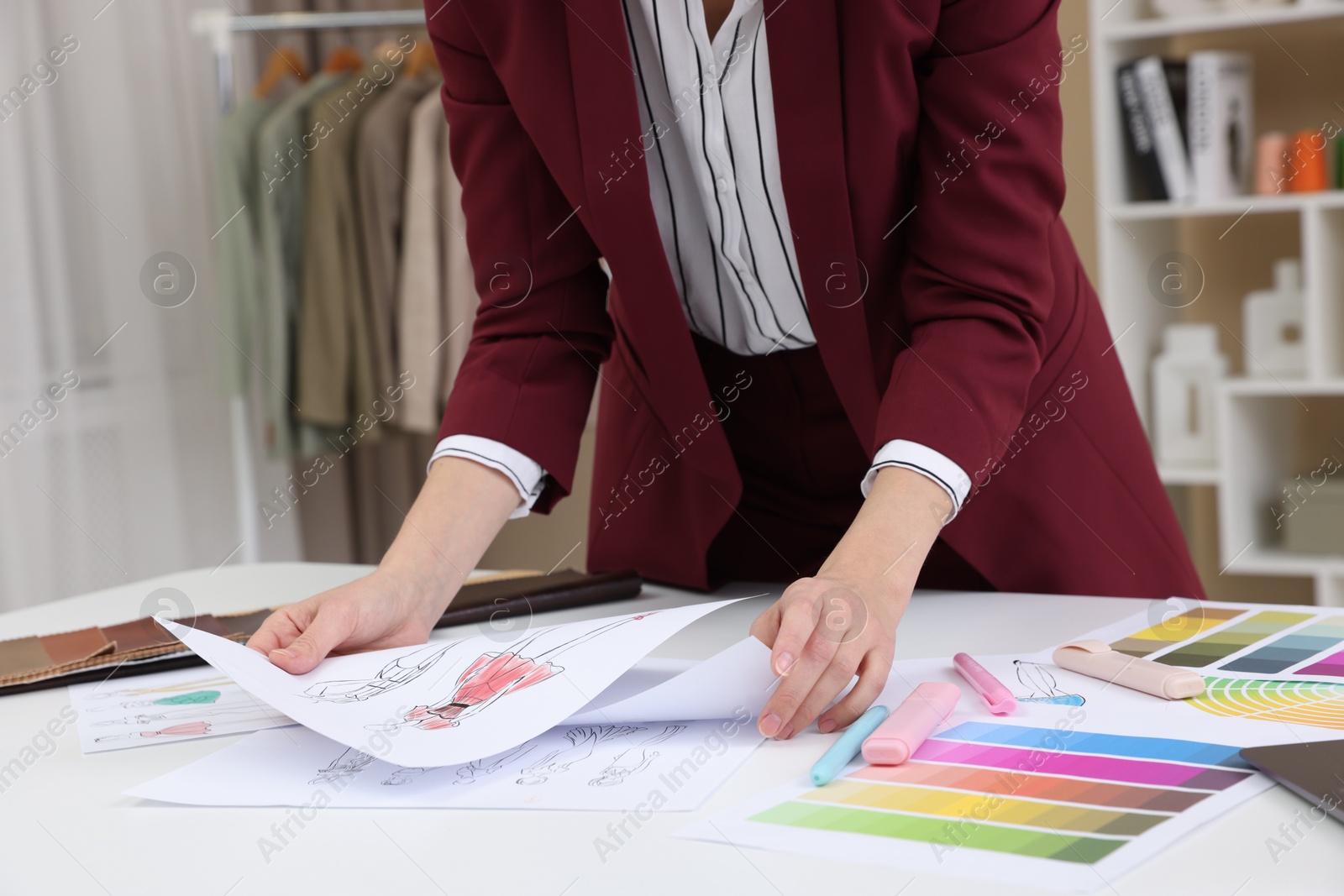 Photo of Fashion designer with sketches of clothes and color palettes working at white table in workshop, closeup