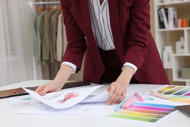 Photo of Fashion designer with sketches of clothes and color palettes working at white table in workshop, closeup