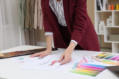 Photo of Fashion designer with sketches of clothes and color palettes working at white table in workshop, closeup