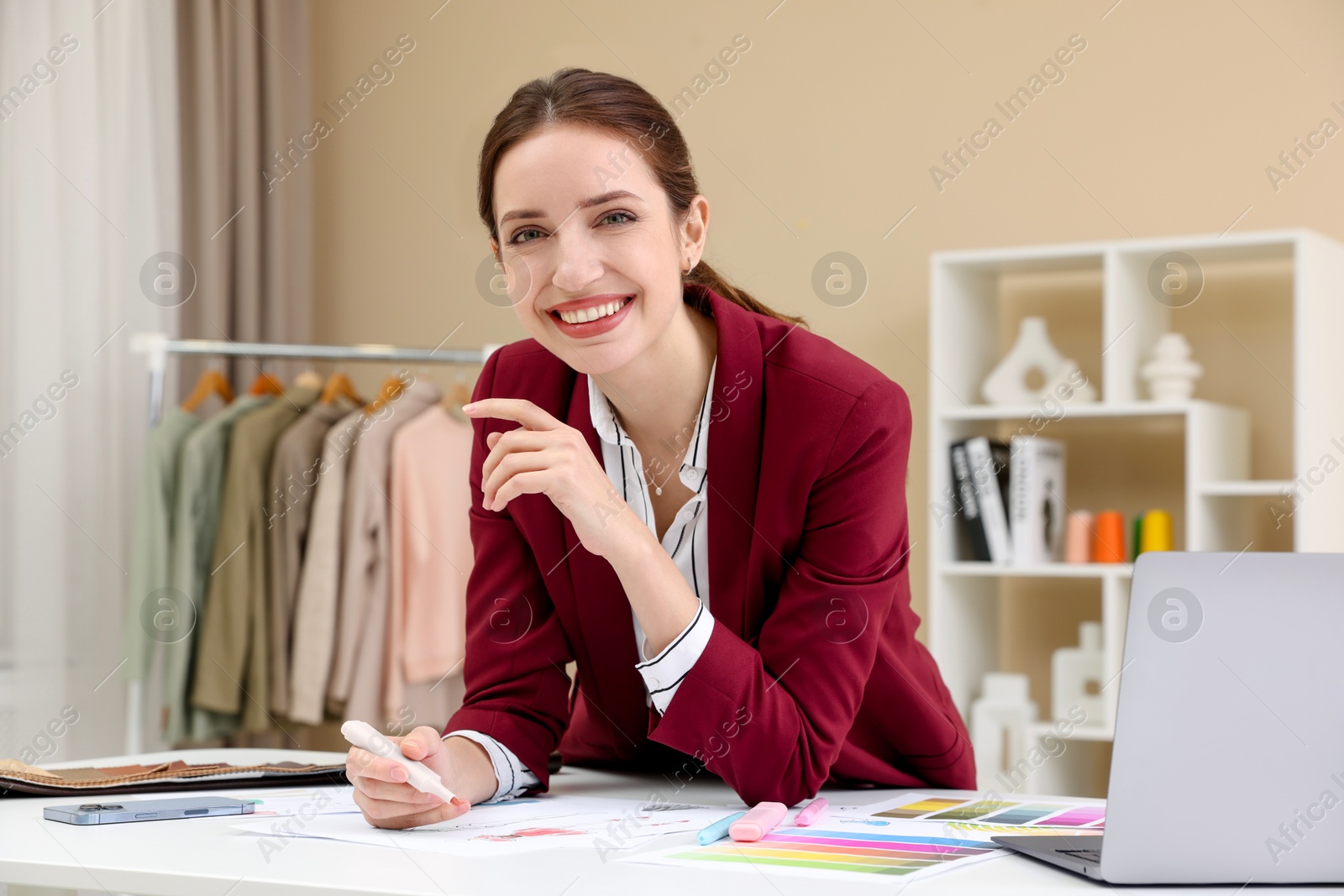 Photo of Fashion designer drawing sketch of clothes at white table in workshop