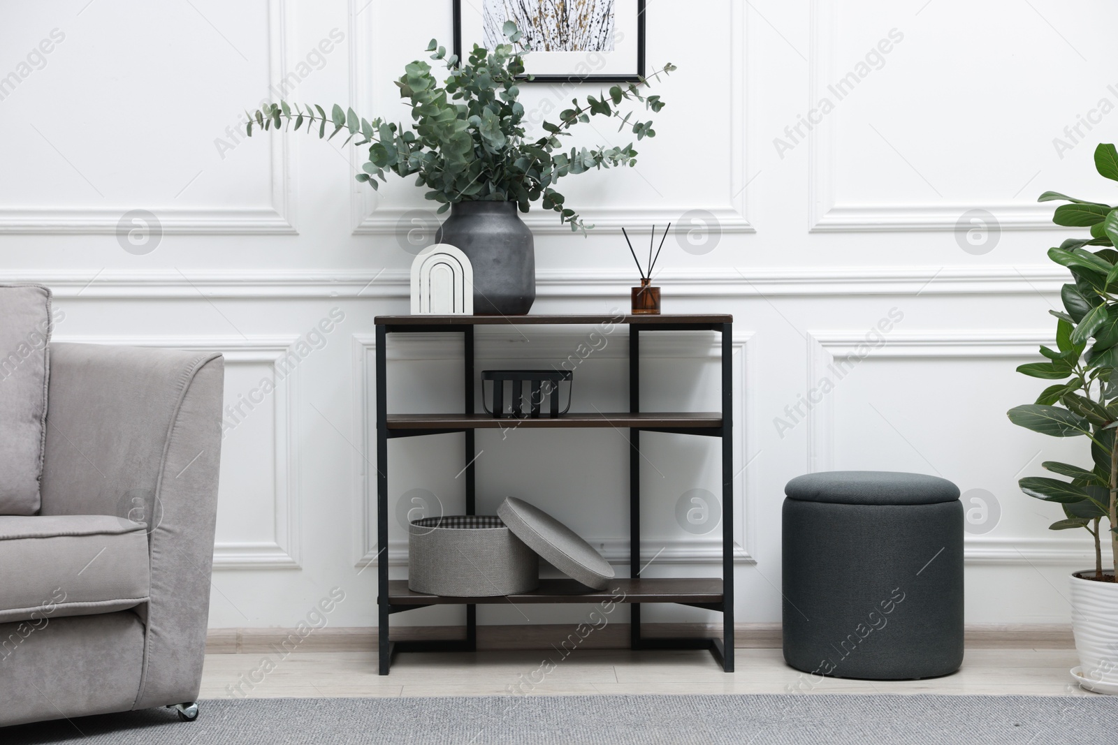 Photo of Console table with decor, houseplant, pouf and armchair near white wall in room. Interior design