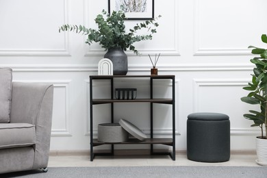 Photo of Console table with decor, houseplant, pouf and armchair near white wall in room. Interior design