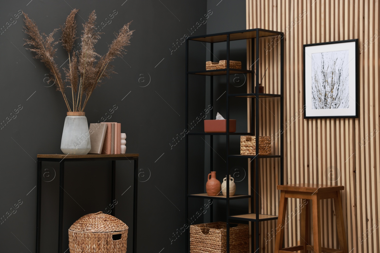 Photo of Console table with decor, shelving unit and stool near grey wall in room. Interior design