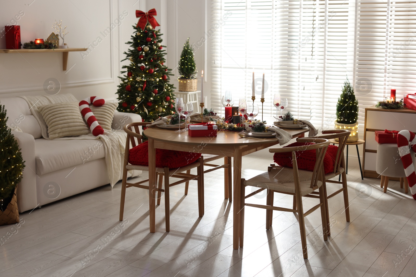 Photo of Christmas table setting with stylish dishware, glasses and burning candles in festive decorated room