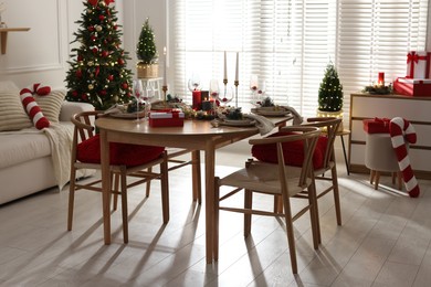 Photo of Christmas table setting with stylish dishware, glasses and burning candles in festive decorated room