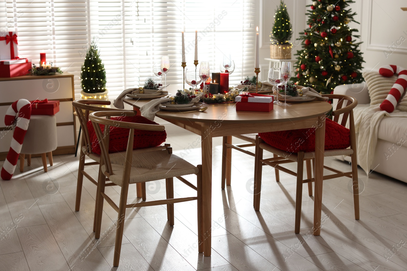 Photo of Christmas table setting with stylish dishware, glasses and burning candles in festive decorated room