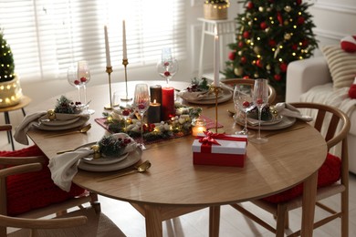 Photo of Christmas table setting with stylish dishware, glasses and burning candles in festive decorated room