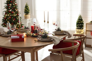 Photo of Christmas table setting with stylish dishware, glasses and burning candles in festive decorated room