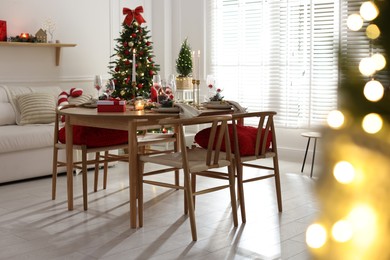 Photo of Christmas table setting with stylish dishware, glasses and burning candles in festive decorated room