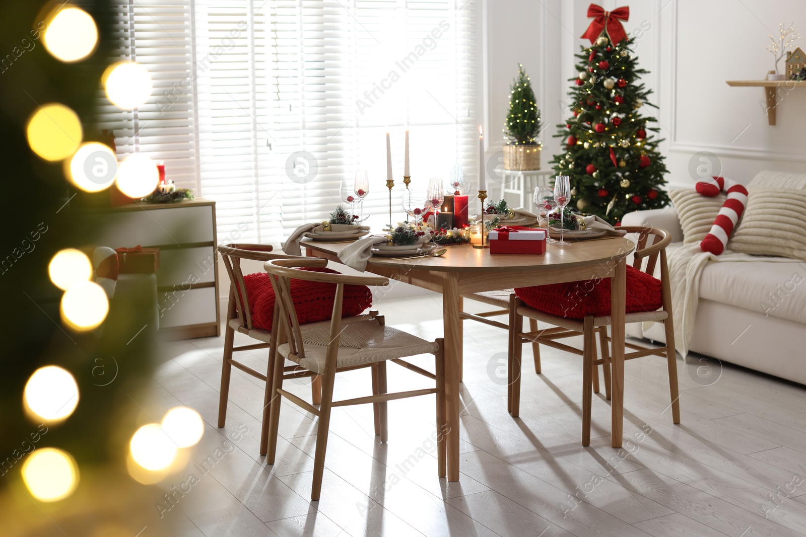 Photo of Christmas table setting with stylish dishware, glasses and burning candles in festive decorated room