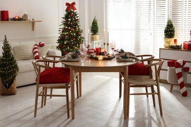 Photo of Christmas table setting with stylish dishware, glasses and burning candles in festive decorated room