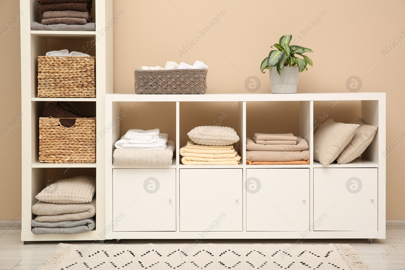 Photo of Folded linens and pillows on shelving unit indoors. Home textile storage