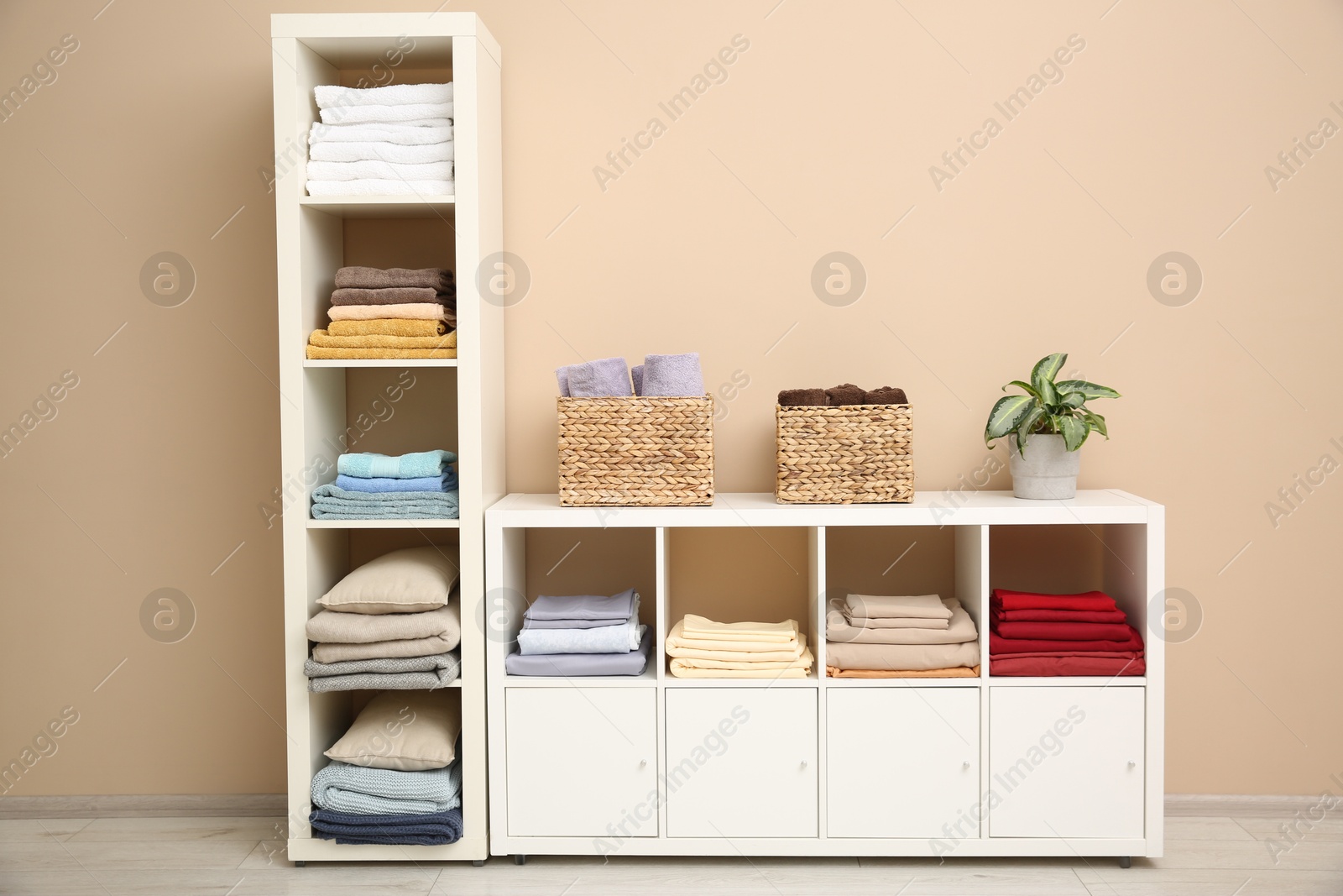 Photo of Folded linens, towels and pillows on shelving unit near beige wall. Home textile storage