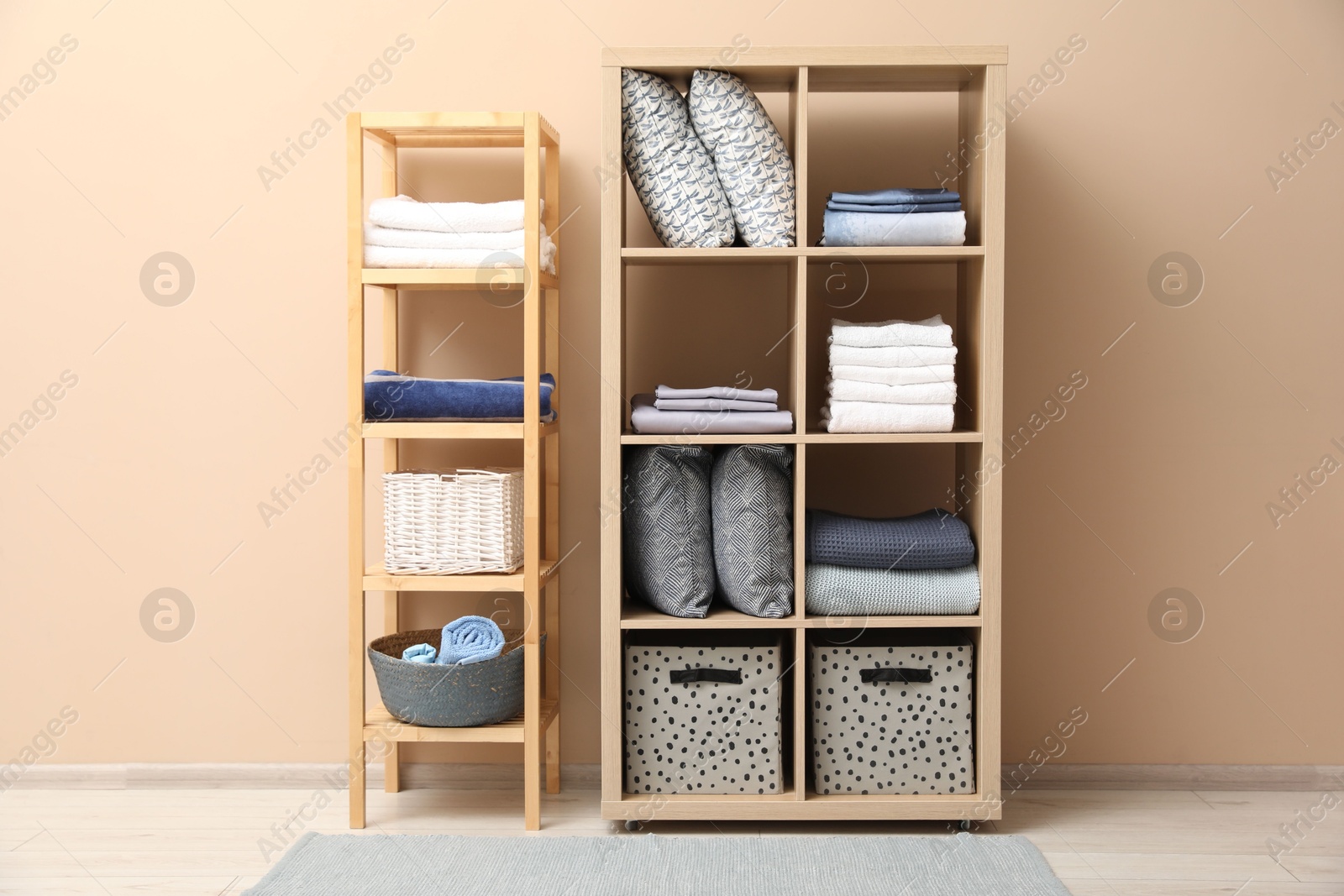 Photo of Home textile organization. Different pillows, linens towels and blankets on shelving units near beige wall