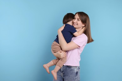 Happy mother with her cute little son on light blue background, space for text