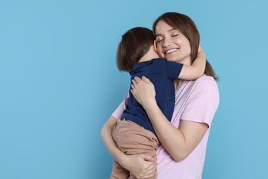 Happy mother with her cute little son on light blue background, space for text