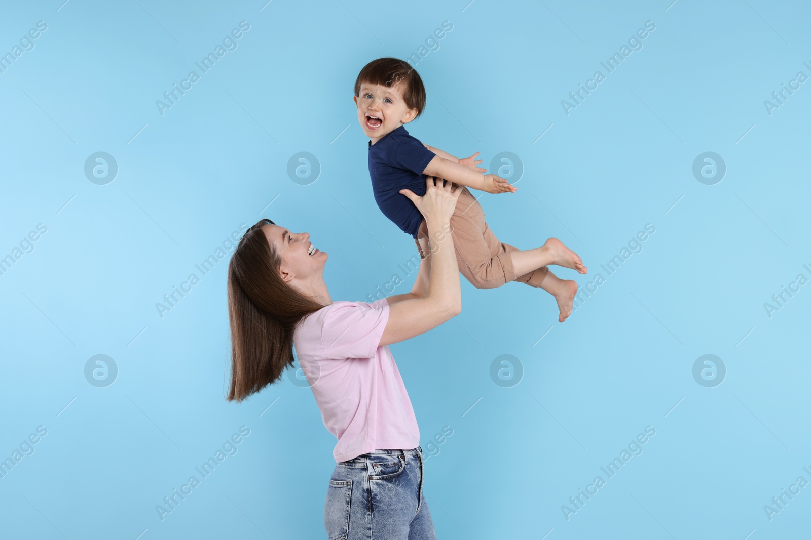 Photo of Happy mother having fun with her cute little son on light blue background