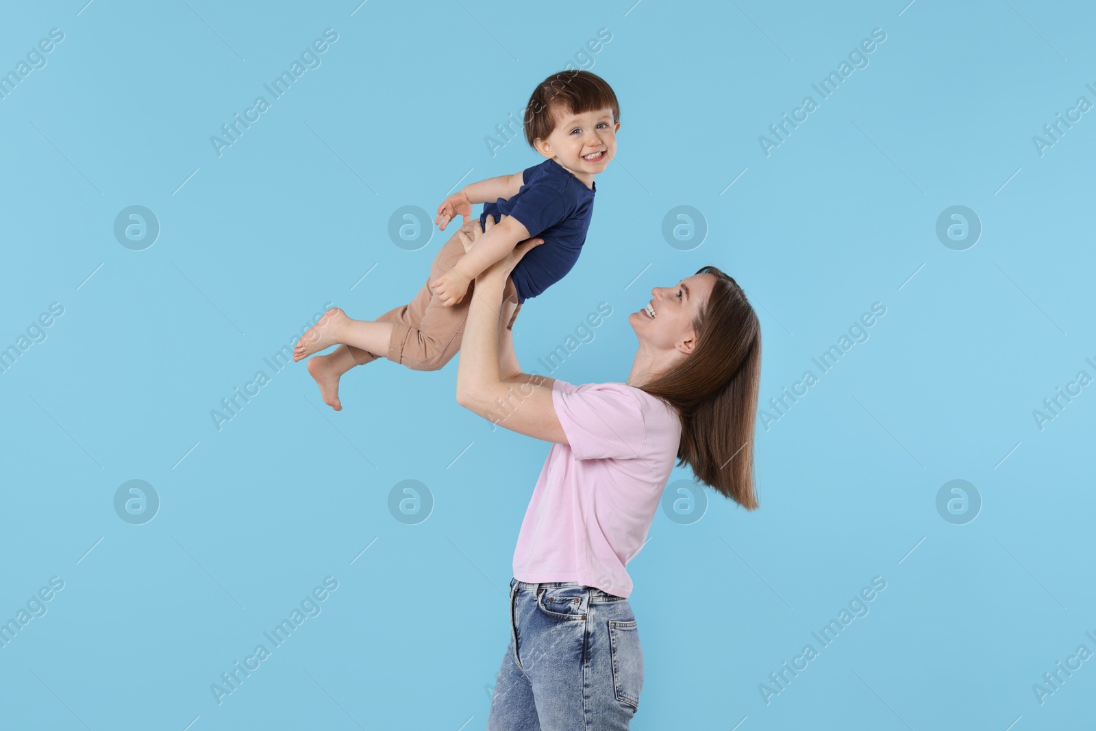 Photo of Happy mother having fun with her cute little son on light blue background