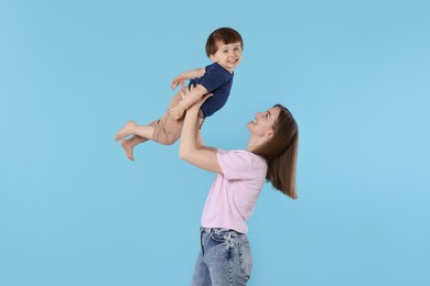 Happy mother having fun with her cute little son on light blue background