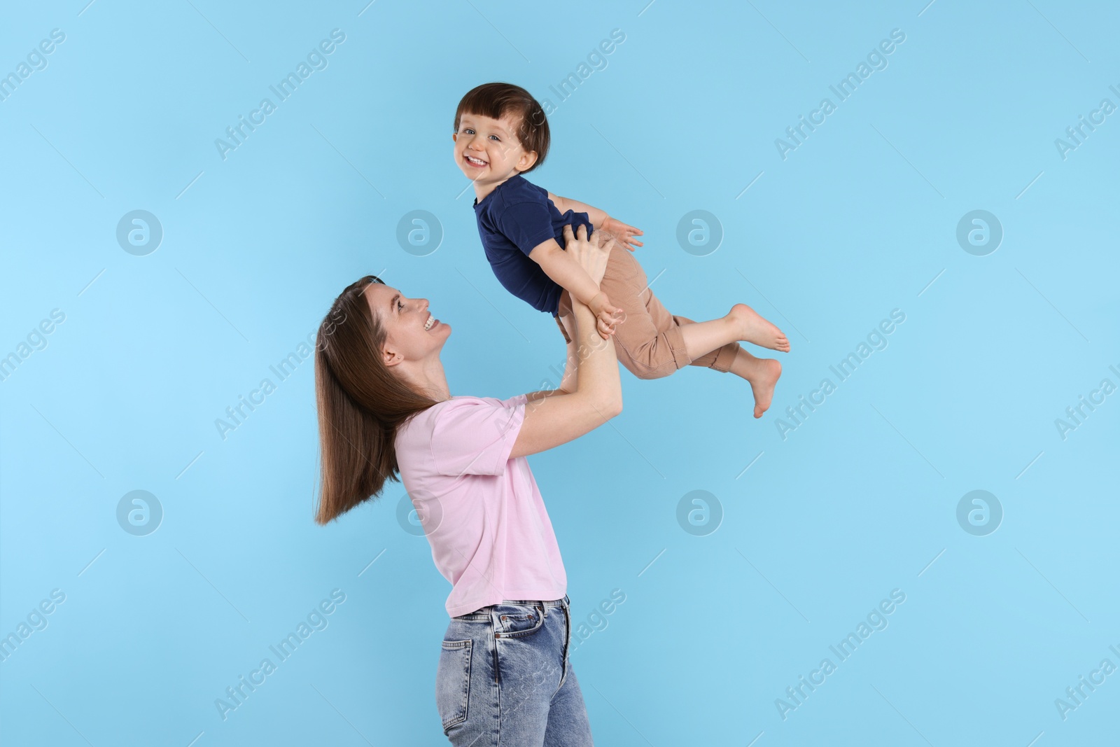 Photo of Happy mother having fun with her cute little son on light blue background