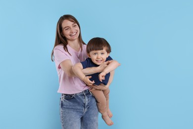 Photo of Happy mother with her cute little son on light blue background, space for text