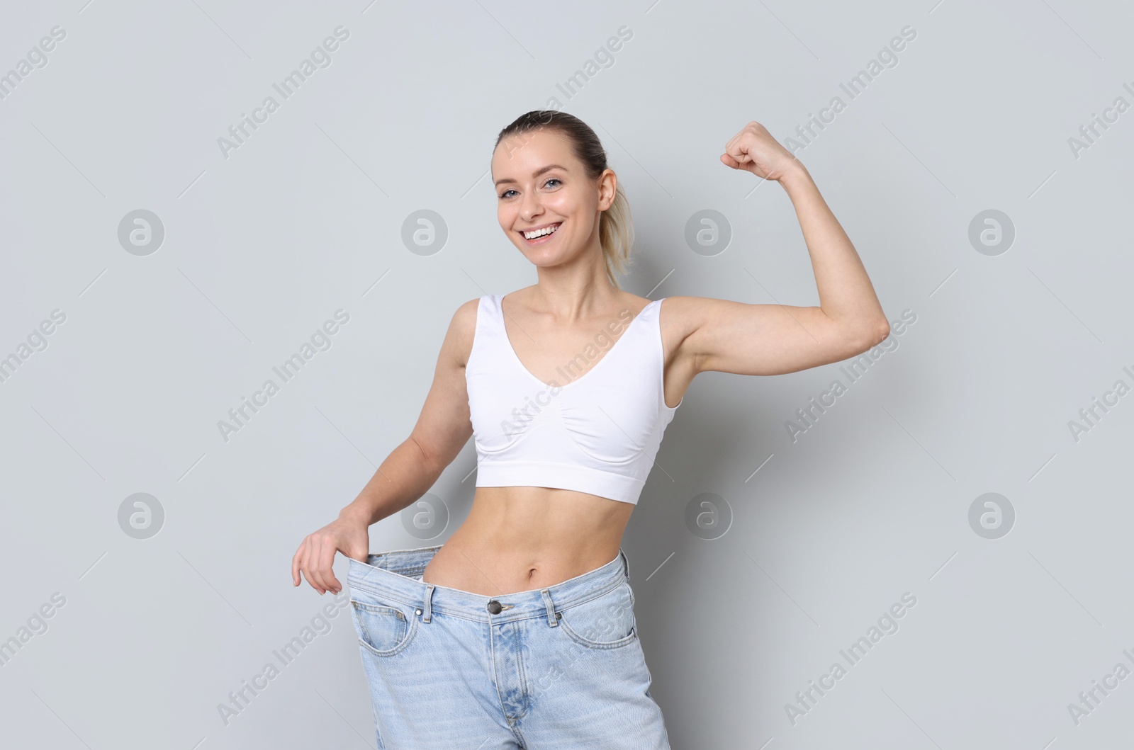 Photo of Weight loss. Happy woman wearing big jeans on light grey background