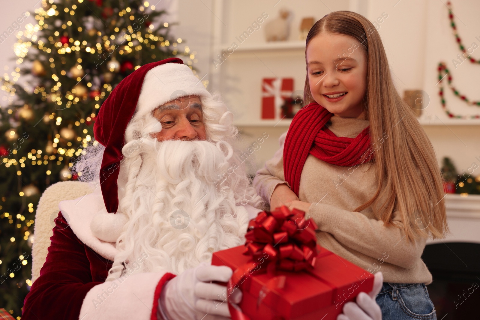 Photo of Christmas celebration. Santa Claus giving gift box to girl at home