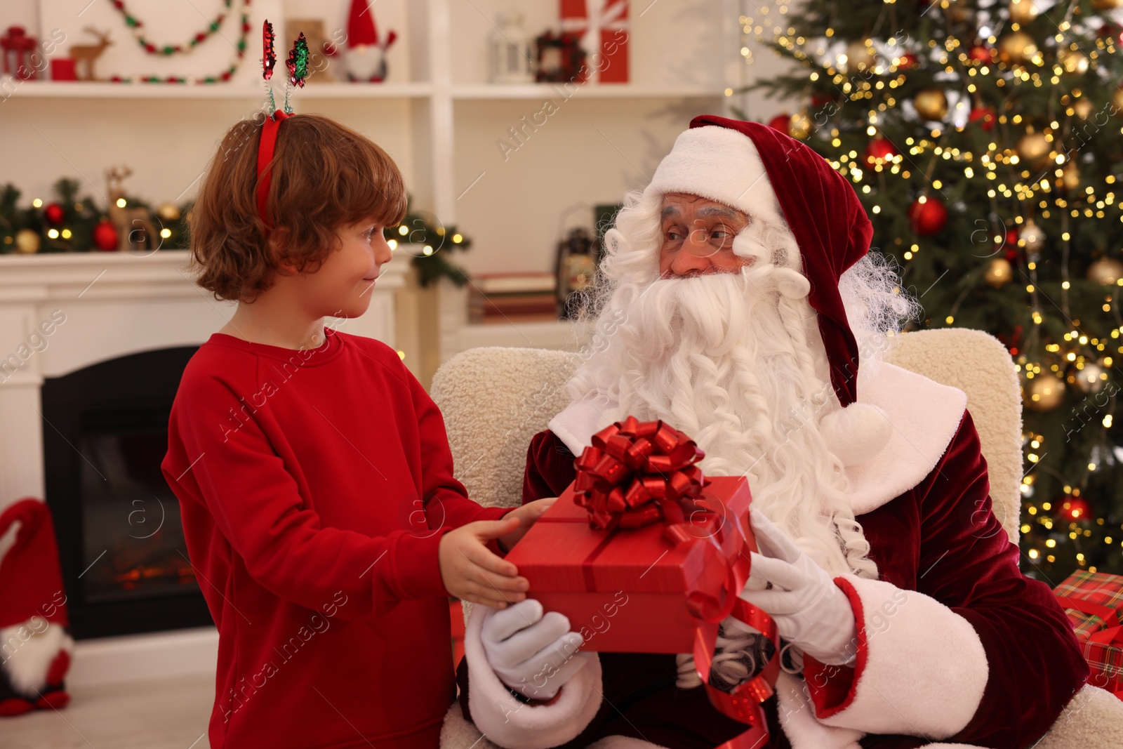 Photo of Christmas celebration. Santa Claus giving gift box to boy at home