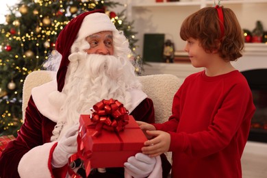 Photo of Christmas celebration. Santa Claus giving gift box to boy at home