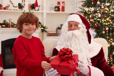 Photo of Christmas celebration. Santa Claus giving gift box to boy at home