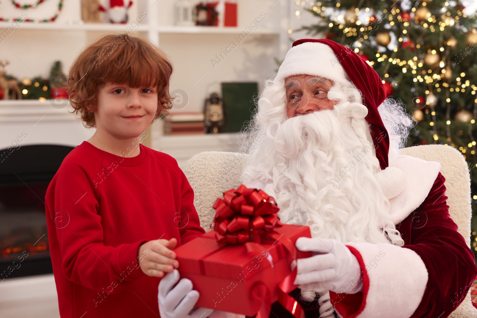 Photo of Christmas celebration. Santa Claus giving gift box to boy at home