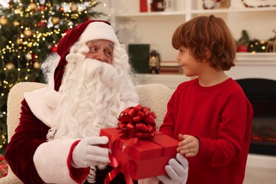 Photo of Christmas celebration. Santa Claus giving gift box to boy at home