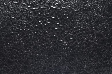 Photo of Water drops on dark grey glass surface, top view