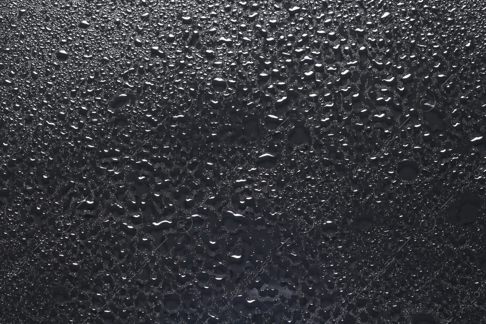 Photo of Water drops on dark grey glass surface, top view