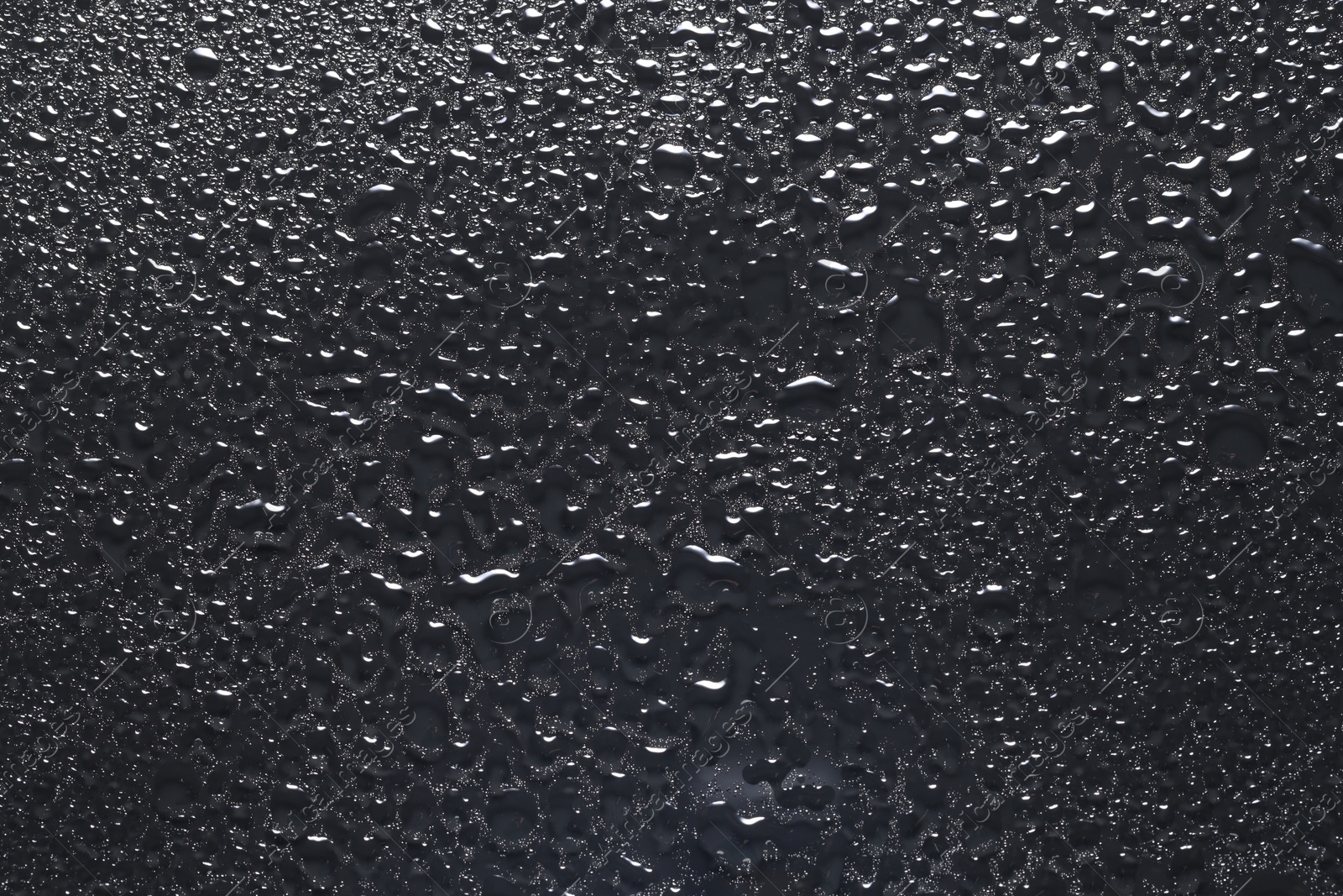 Photo of Water drops on dark grey glass surface, top view