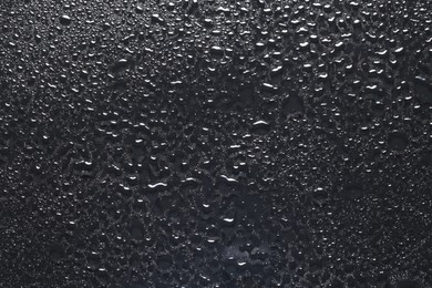 Photo of Water drops on dark grey glass surface, top view