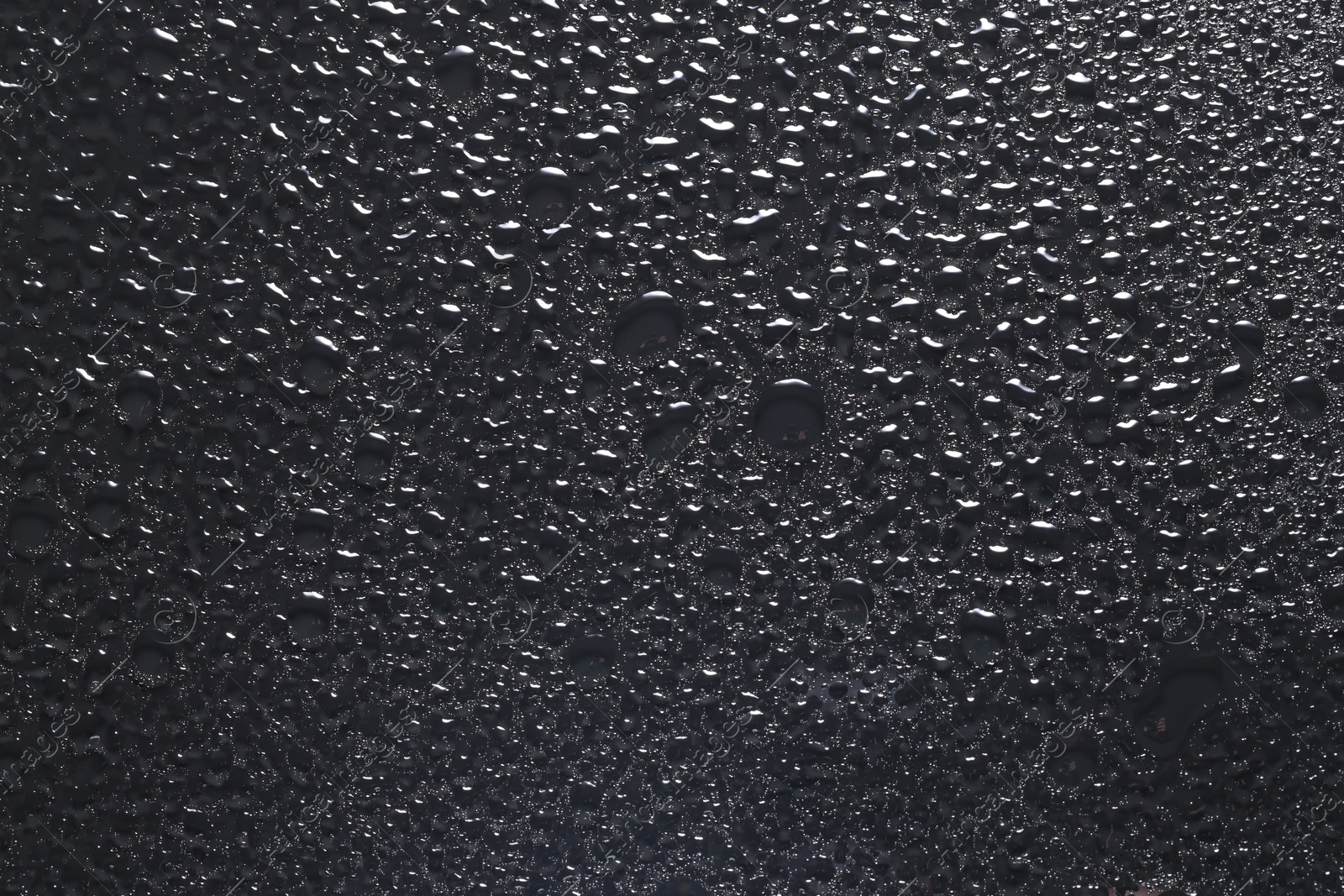 Photo of Water drops on dark grey glass surface, top view