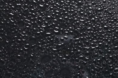 Photo of Water drops on dark grey glass surface, top view