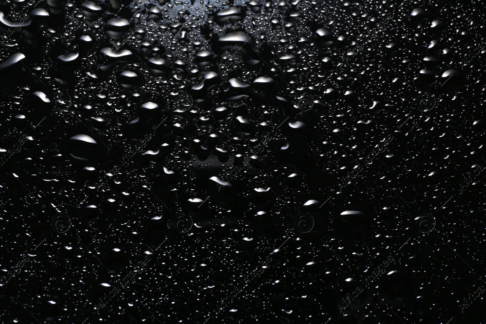 Photo of Water drops on black glass surface, top view