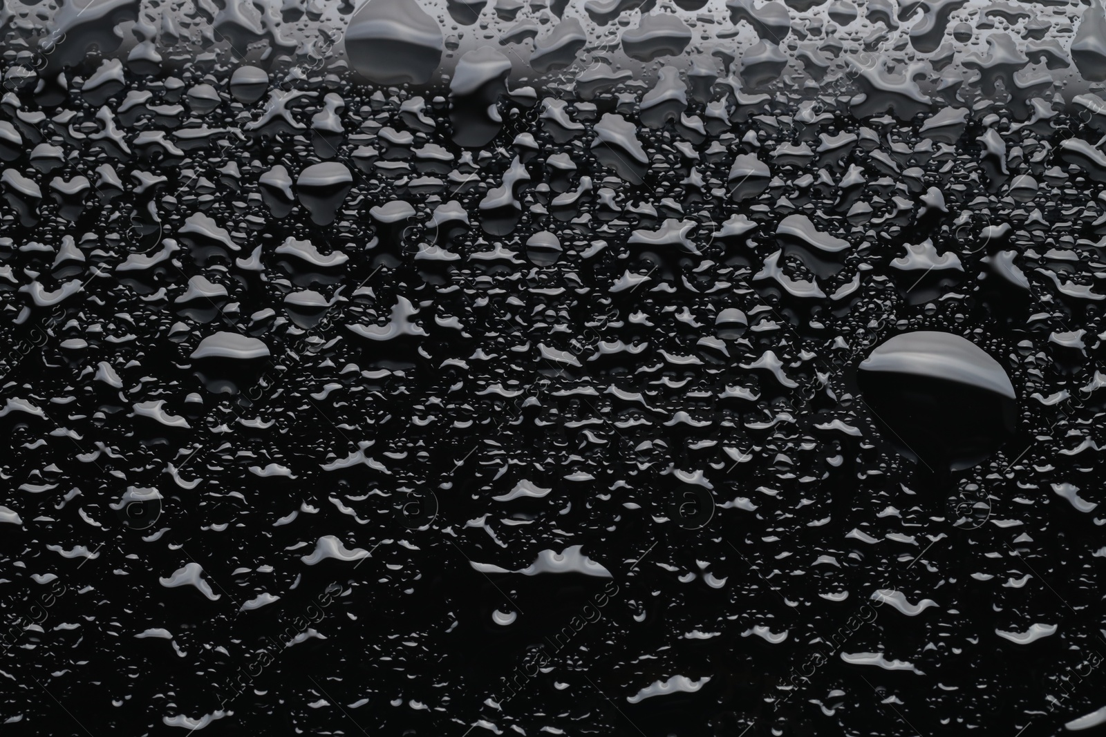 Photo of Water drops on black glass surface, top view