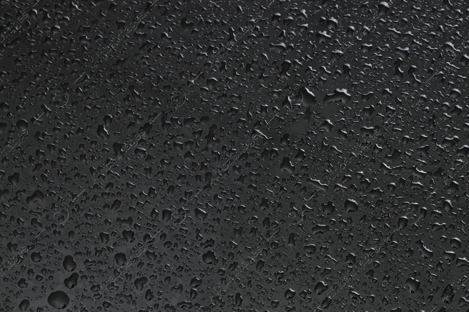 Photo of Water drops on dark grey glass surface, top view