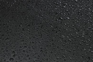 Photo of Water drops on dark grey glass surface, top view