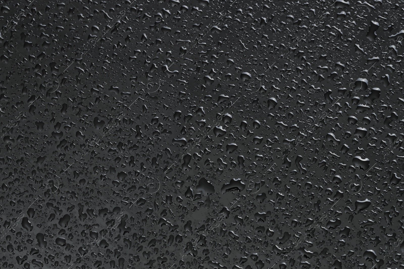 Photo of Water drops on dark grey glass surface, top view